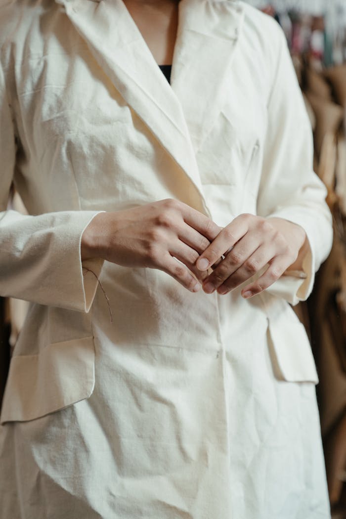 Hands of a person adjusting a light-colored jacket in a sewing workshop.