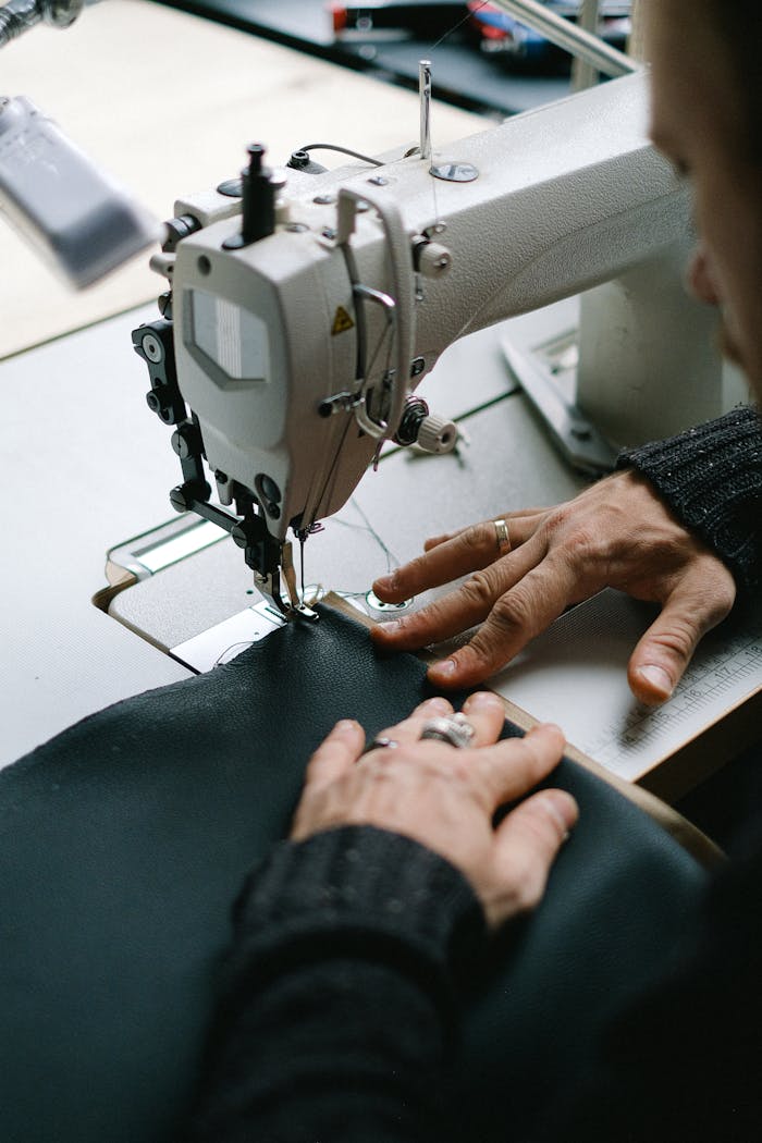 Close-up of a tailor skillfully sewing fabric with a sewing machine in a workshop setting.